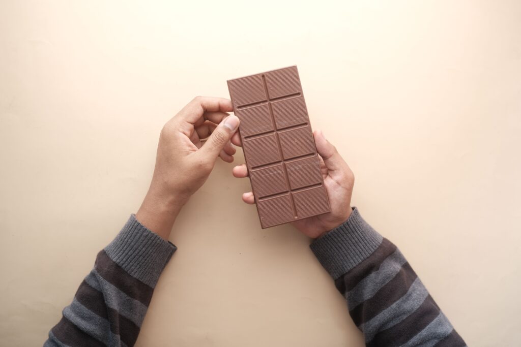 Close-up of hands holding a chocolate bar with a striped sweater, captured in natural light.