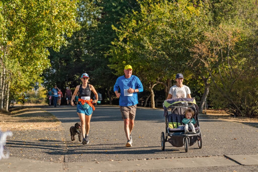 A group of people jogging and walking with a stroller on a sunny day in a park.