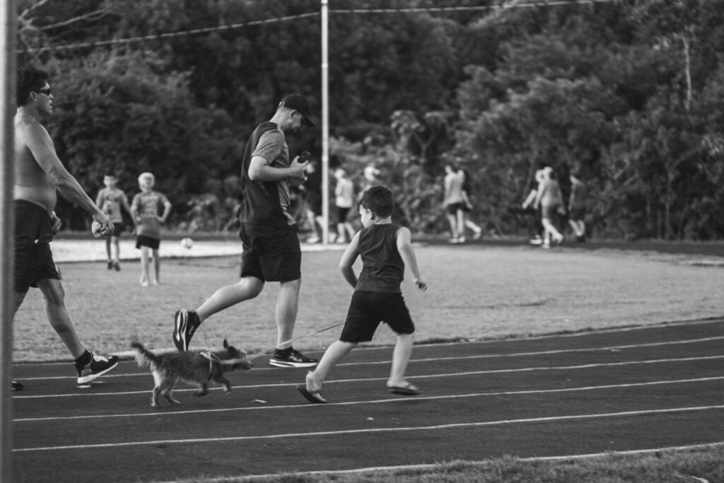 Black and white photo of people jogging with a dog on an outdoor track.