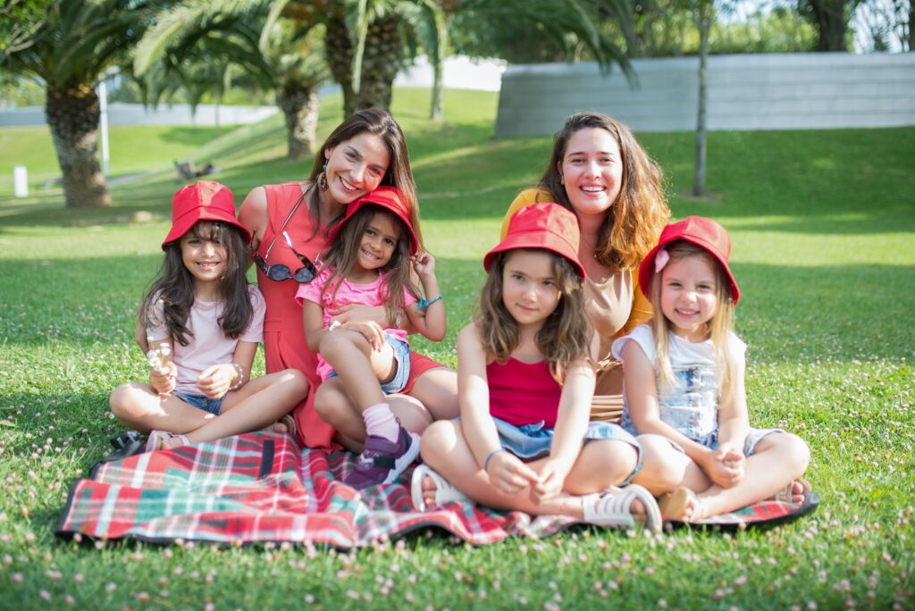 Friends enjoying a sunny day picnic on grass with bucket hats and smiles in a Portuguese park.